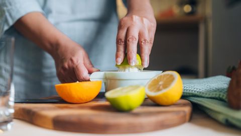 Gros plan sur des mains féminines pressant du citron vert frais dans un presse-citron manuel tout en préparant le petit-déjeuner dans la cuisineGetty Images