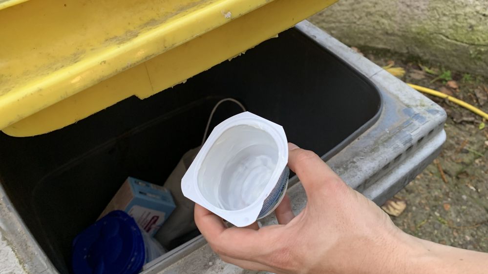 pot de yaourt est déposé dans le bac jaune recyclage des ordures ménagères