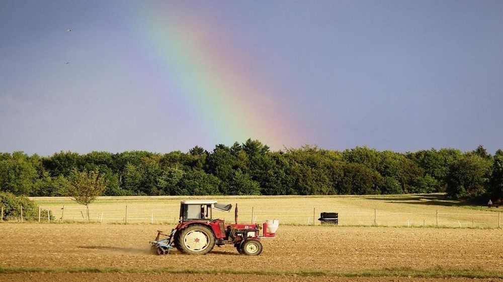 Tracteur labourant un champ sous un arc-en-ciel.