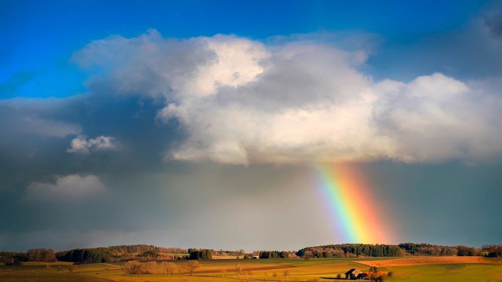 Arc-en-ciel sous un ciel nuageux au-dessus d'un champ Arc-en-ciel sous un ciel nuageux au-dessus d'un champ