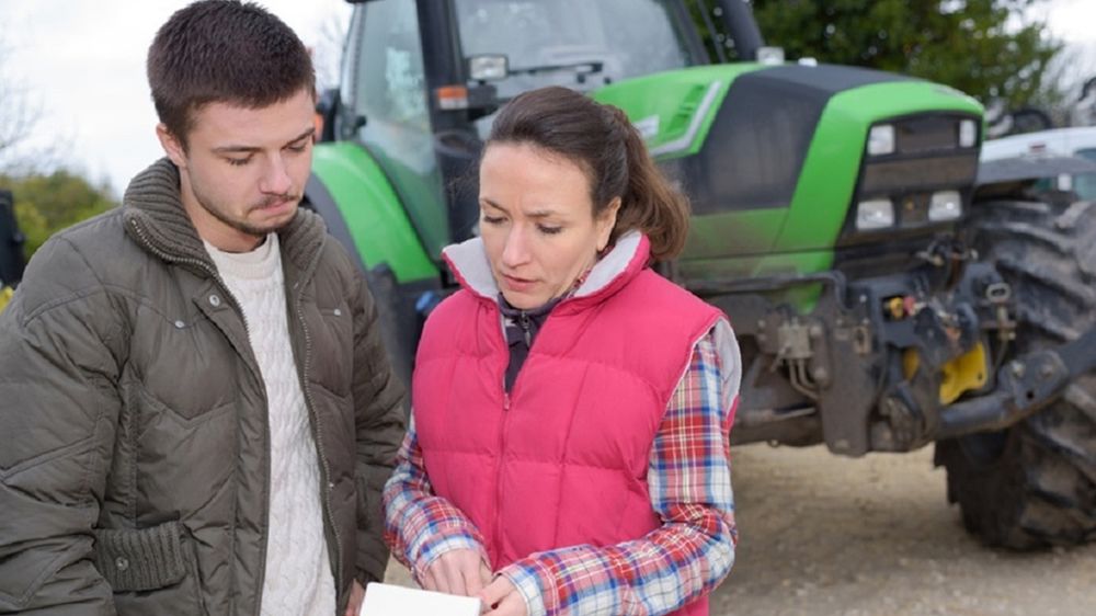 Jeune agriculteur et agricultrice devant un tracteur