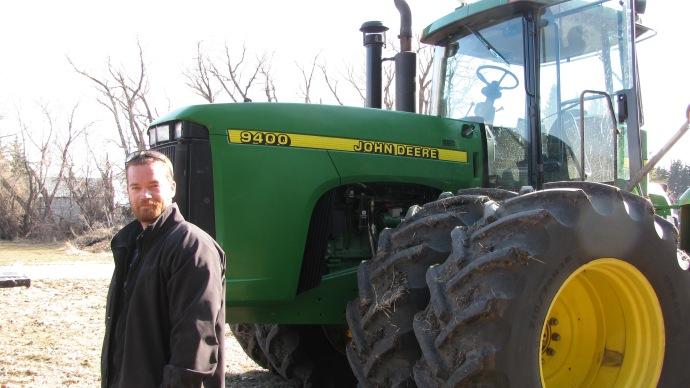 Chris McCallister, agriculteur canadien, devant un tracteur John Deere 9400.