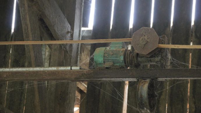 En hauteur, l’éleveur a placé un moteur électrique avec un réducteur et une poulie fendue. Une sangle plate reliée aux deux côtés du cadre s’enroule sur la poulie quand le treuil est actionné.